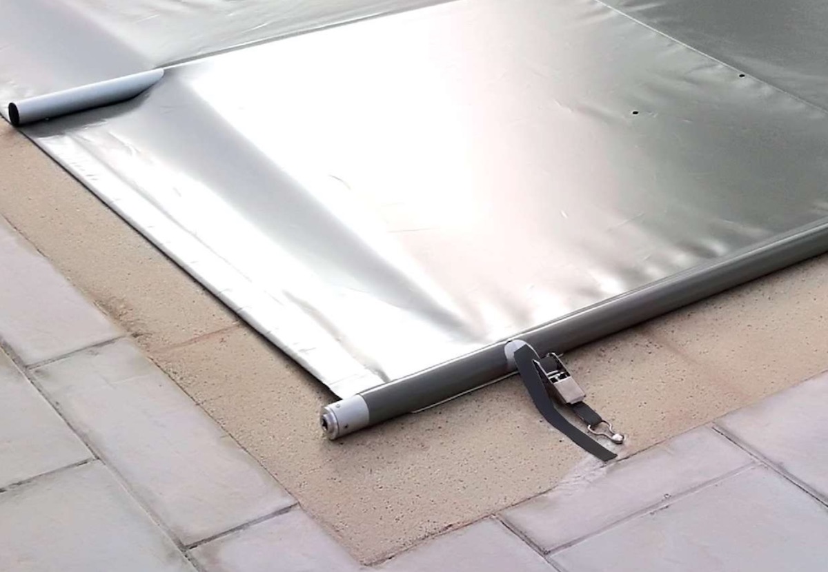 Cobertor de barras gris extendido apoyado sobre el borde de la piscina con sus tensores de carraca colocados para mayor seguridad
