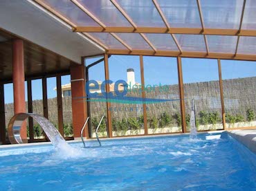 Una espectacular prolongación de la casa para un disfrute todo el año. Interior de cubierta de piscina fija adosada a la casa en Madrid, con estructura de aluminio color madera y techo de policarbonato celular.