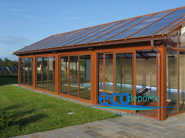 Acristalamiento de piscina climatizada en Asturias con vidrio doble y policarbonato celular. Exterior de cubierta de piscina fija con estructura de aluminio color madera.