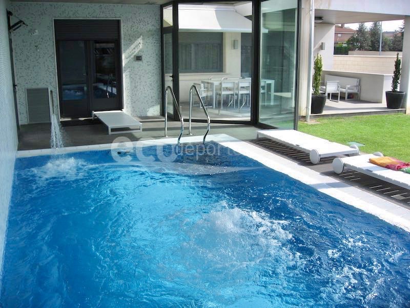 Interior de piscina climatizada desbordante equipada con cañón, masaje de aire de fondo y escalera residencial de acceso fácil. Acceso directo desde el interior de la casa, y acristalada al jardín.