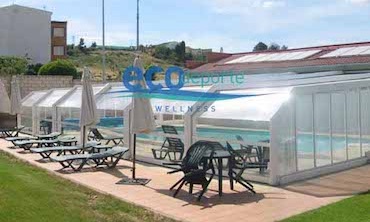 Cubierta adosada telescópica Climatizar piscina con cubierta acristalada móvil adosada a un edificio de vestuarios. Incluye placas solares para el calentamiento del agua de al piscina.