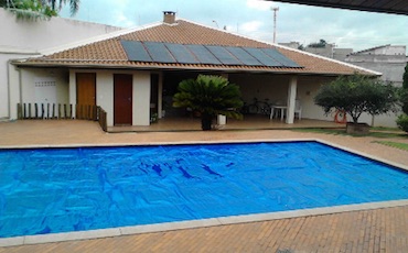Las placas solares calientan el agua y la cubierta térmica evita que se enfríe, sobre todo por la noche Piscina exterior de verano con manta térmica extendida y colectores solares de polipropileno en el tejado de la casa