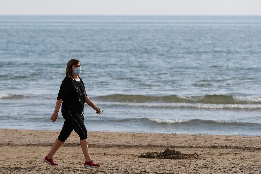 La mascarilla ayuda a prevenir contagios durante nuestros paseos por la playa Mujer paseando por la playa con la mascarilla facial bien colocada