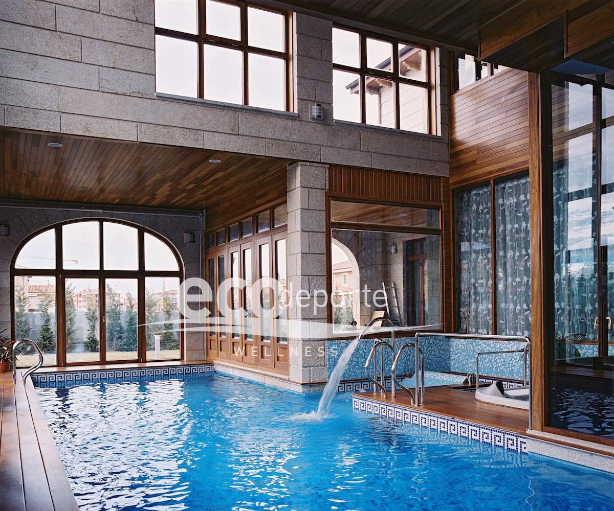Ambiente interior de gran amplitud con ventanales al exterior en las dos alturas. Interior de la piscina climatizada con paredes de piedra natural en Madrid.