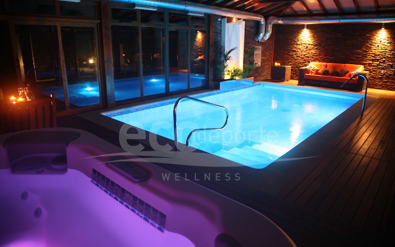 La cromoterapia se refleja en las zonas con acristalamiento doble. Interior nocturno de la cubierta de madera luciendo la cromoterapia en la piscina y el spa.