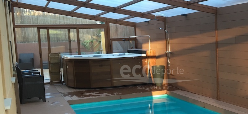 Jacuzzi interior de lujo bajo una cubierta acristalada con los últimos rayos de sol de la tarde. Jacuzzi interior grande en esquina dentro de un techo acristalado con policarbonato celular